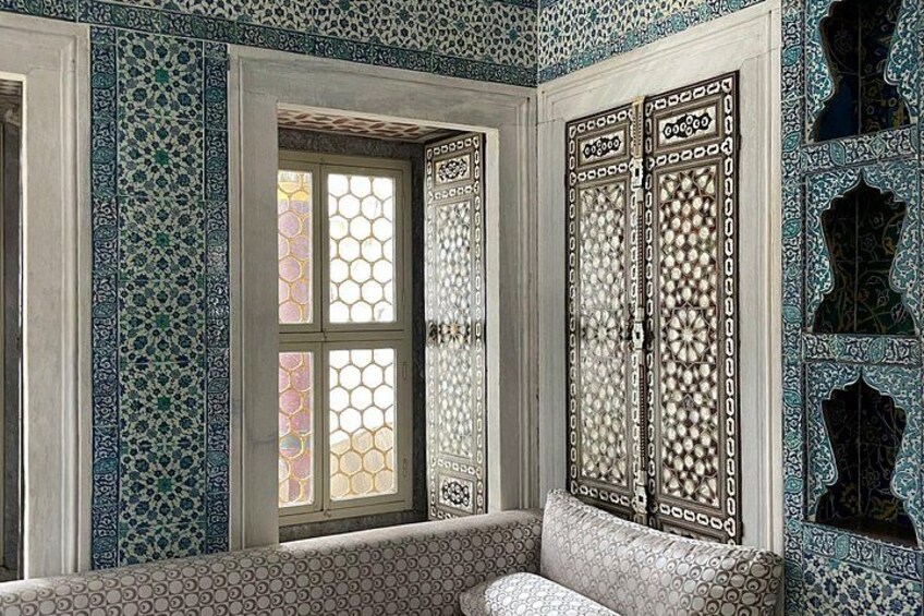 A room with intricate tile work, a window with stained glass, and a bench. 4