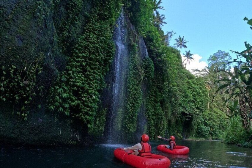 Two people rafting down a river with a waterfall in the background. 2