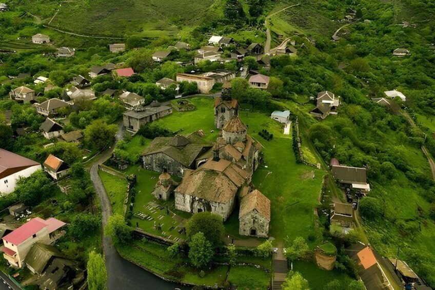 An aerial view of a historic village with a prominent church, narrow roads, and surrounding greenery. 4
