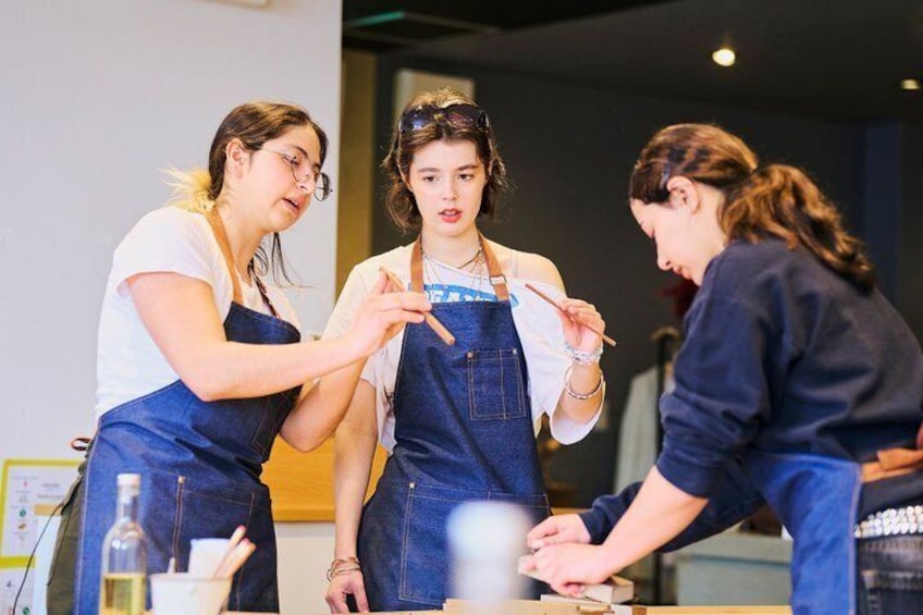 Three people wearing aprons, one in the center, and two on the sides, engaged in a discussion or activity at a table. 2