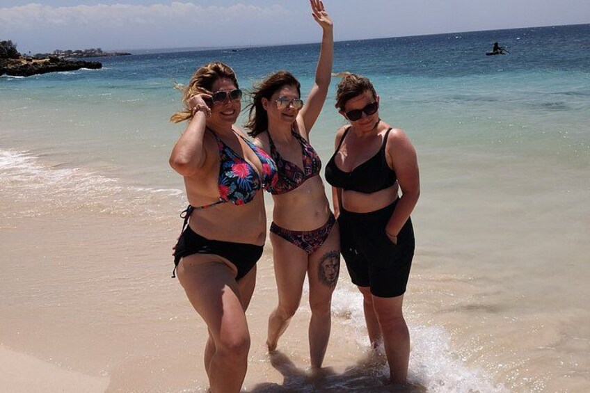Three people walking on a beach with clear water and a rocky shoreline in the background. 4