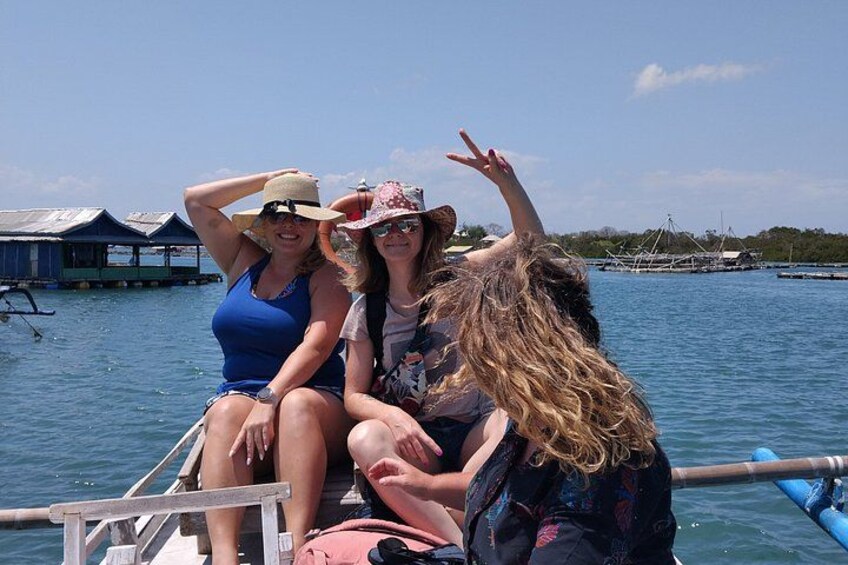 Three people on a boat with water and overwater structures in the background. 1