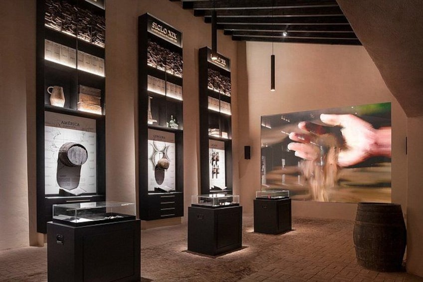A museum interior with display cases, a large projection screen, and a wooden barrel. 4