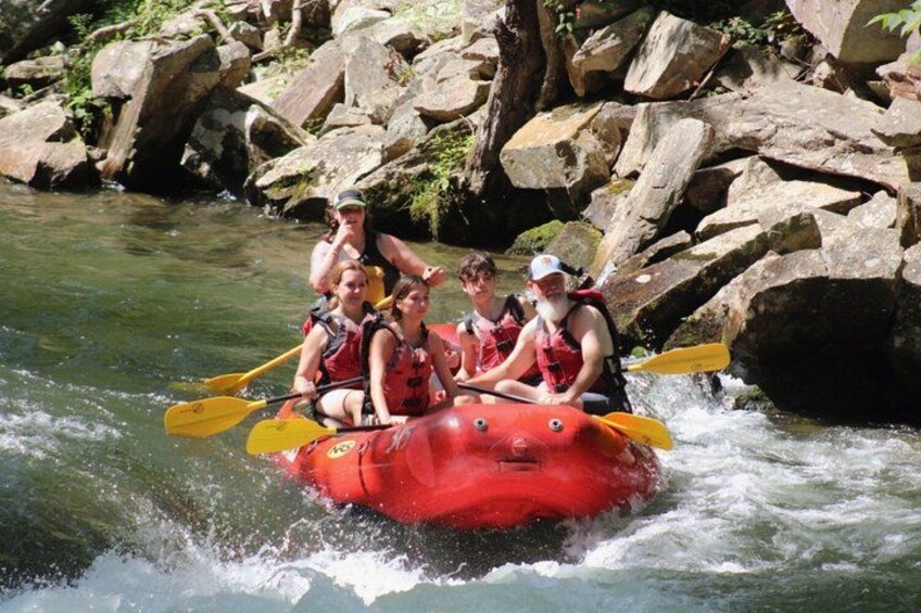A group of people in a red raft navigating a river with rapids, surrounded by rocks and greenery. 2