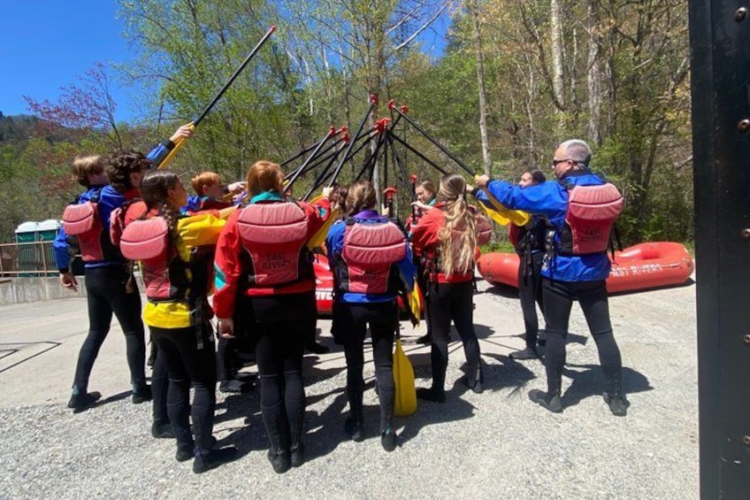 A group of people in outdoor gear, some with backpacks, gathered around a tripod with cameras. 3