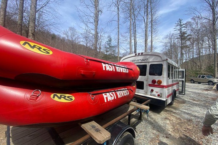 Red kayaks with 'FAST RIVERS' and 'NRS' logos, a white bus labeled 'FAST RIVERS,' and a forested background. 5