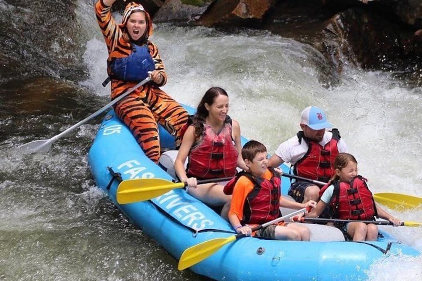 A group of people in a blue inflatable raft on a river with rapids. 4