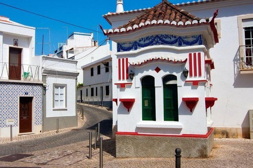A white building with a red and white facade, a tiled roof, and a narrow street. 3