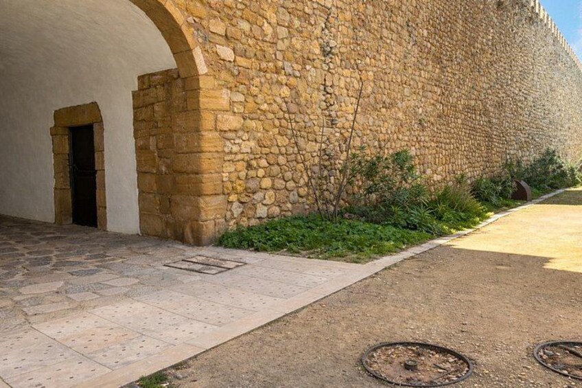 A stone wall with a doorway, a paved path, and some greenery. 5