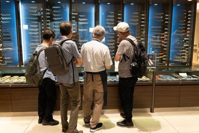 A group of people examining a display of knives in a store. 3