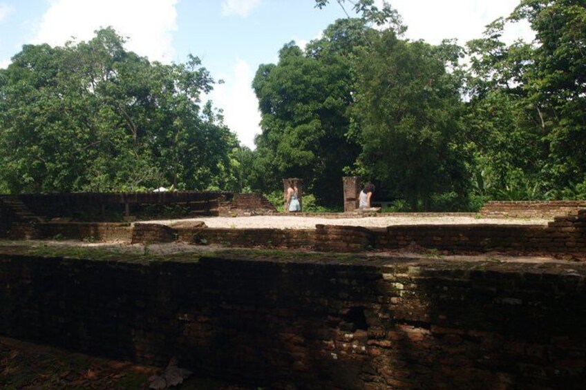 An ancient stone structure with a platform, surrounded by dense green trees. 5