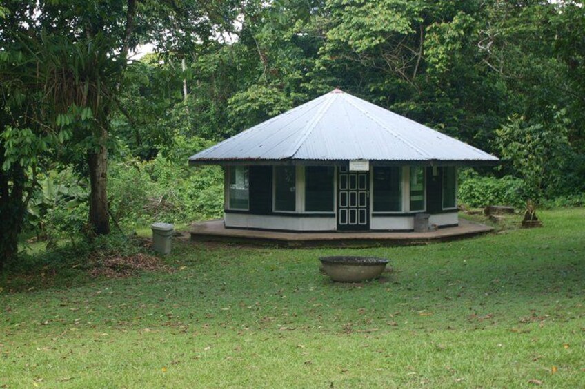 A small, single-story building with a metal roof, surrounded by lush greenery. 4