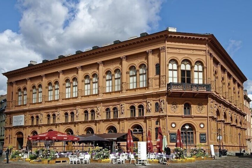 En historisk bygning med detaljeret arkitektur, store vinduer og udendørs siddepladser. 5