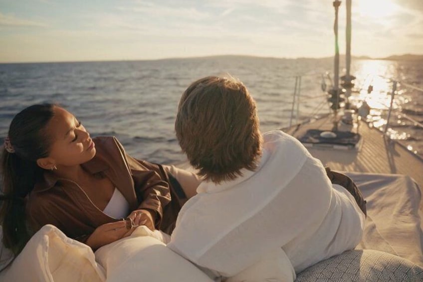 Two people sitting on a boat with a body of water and a pier in the background. 1