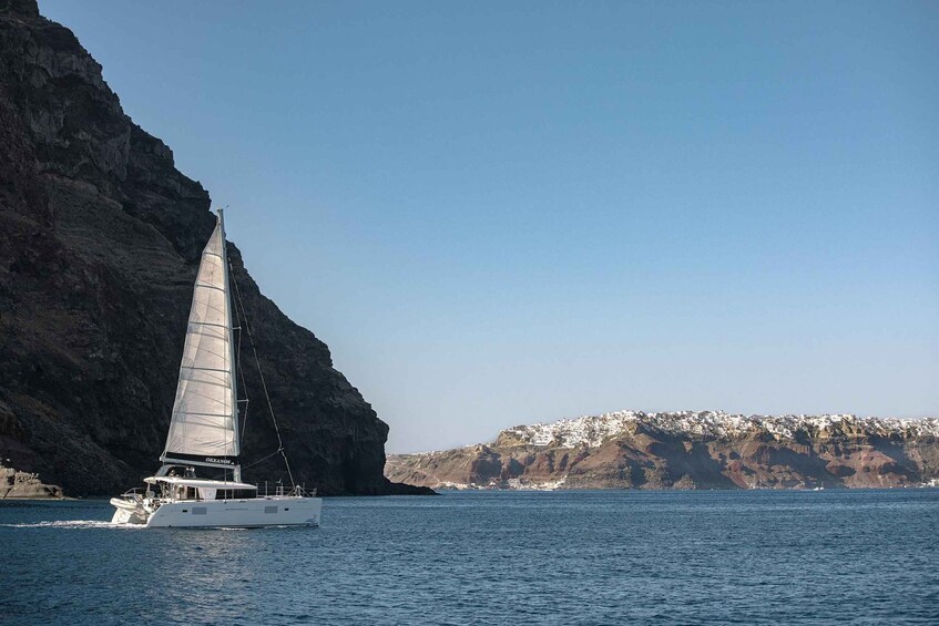 A sailboat on calm waters near a rocky coastline with a village in the background. 1