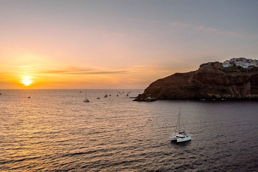 A sunset over a coastal area with boats and a cliff with buildings. 2