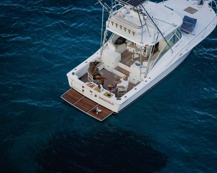 A white yacht named 'Miracolo' with a wooden deck, seating area, and a small cabin. 1