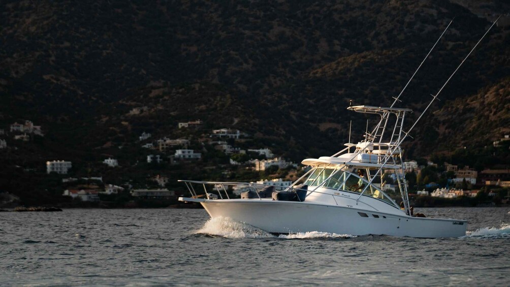 A white boat with a cabin and a mast, moving on calm water with a mountainous coastline in the background. 5