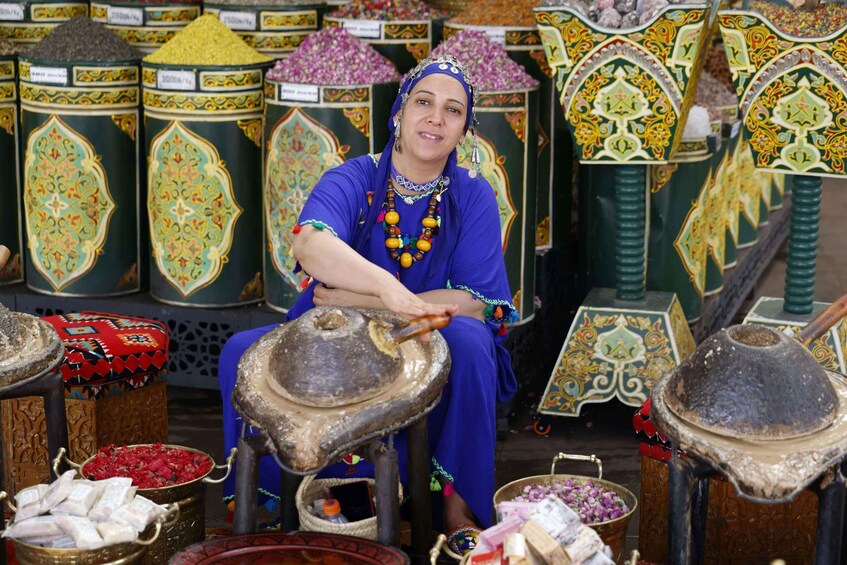 A person in traditional attire sitting at a table with a large clay pot, surrounded by various containers of spices and grains. 4