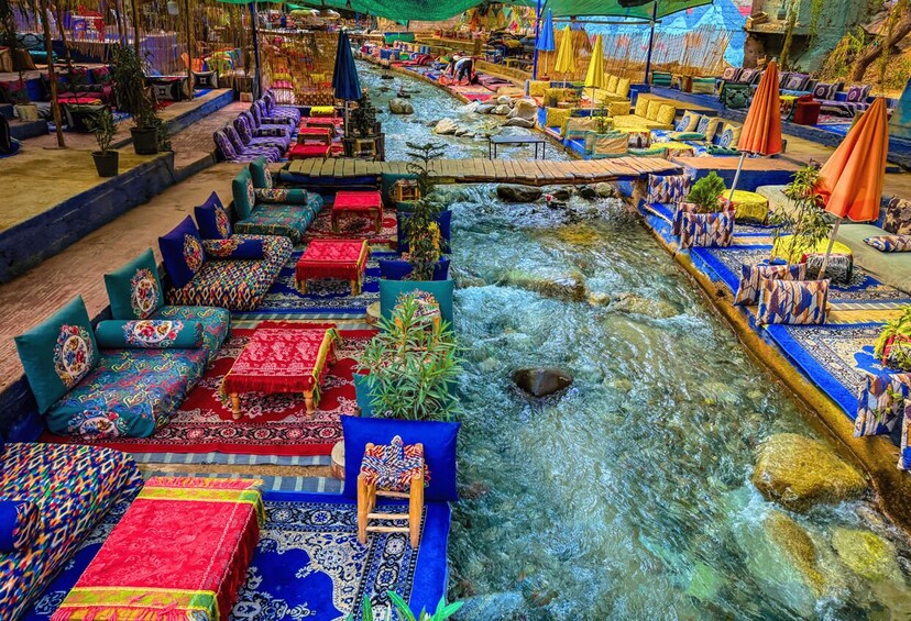 A riverside seating area with colorful textiles and a flowing stream. 3