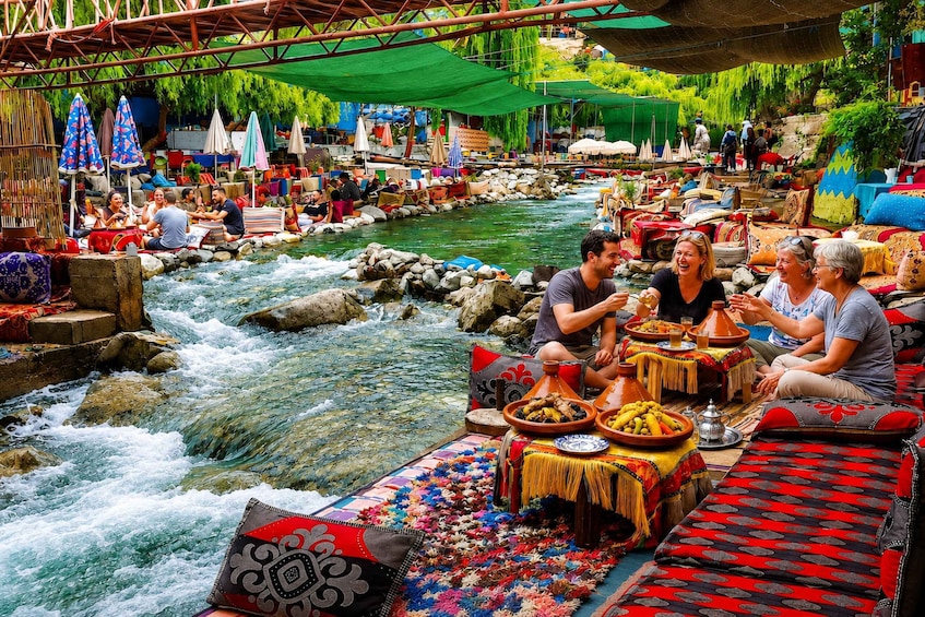 A group of people dining by a flowing river, with colorful textiles and traditional dishes. 1
