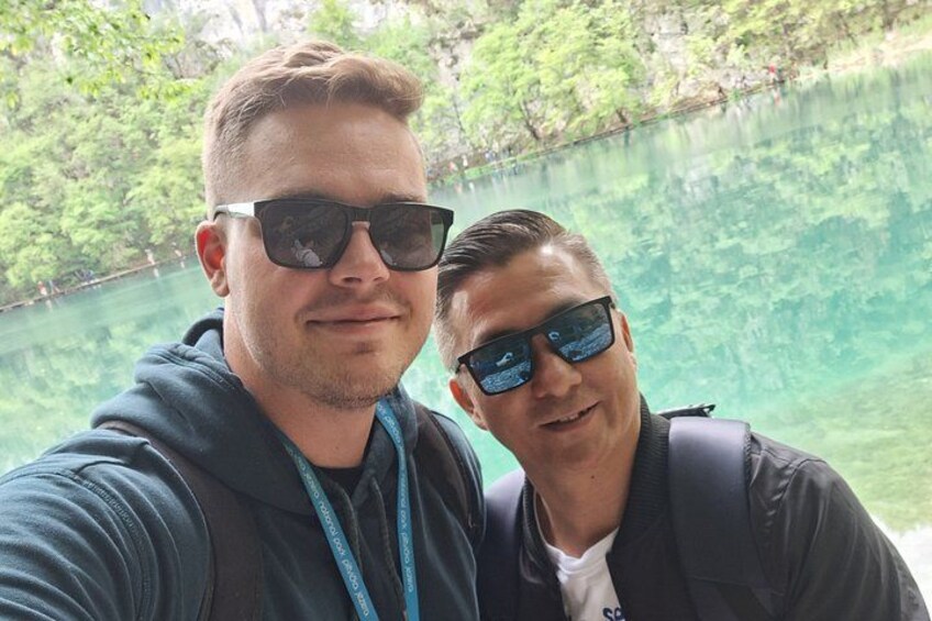 Two individuals near a body of water with trees in the background. 3
