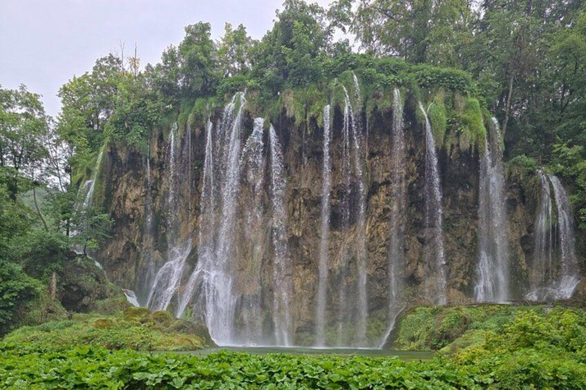 A waterfall cascading down a cliff surrounded by lush greenery. 1
