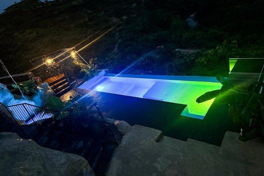 A swimming pool with a waterfall feature, surrounded by rocks and vegetation. 2