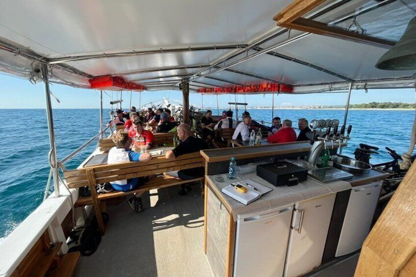 A boat with people dining under a canopy, a kitchen area, and the sea in the background. 2