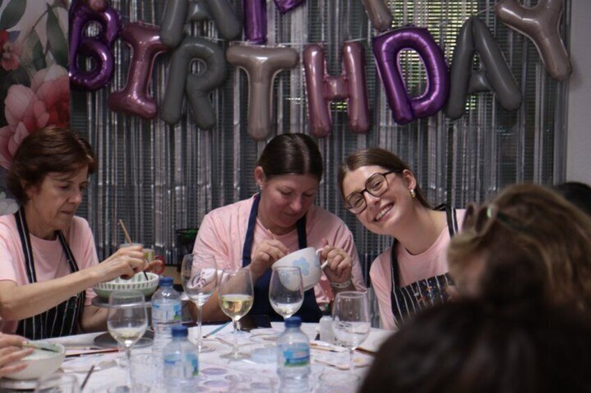 Un grupo de personas sentadas a una mesa con globos que deletrean 'BIRTHDAY' al fondo. 2