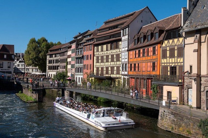 A river with a boat carrying passengers, a bridge, and colorful buildings along the riverbank. 5