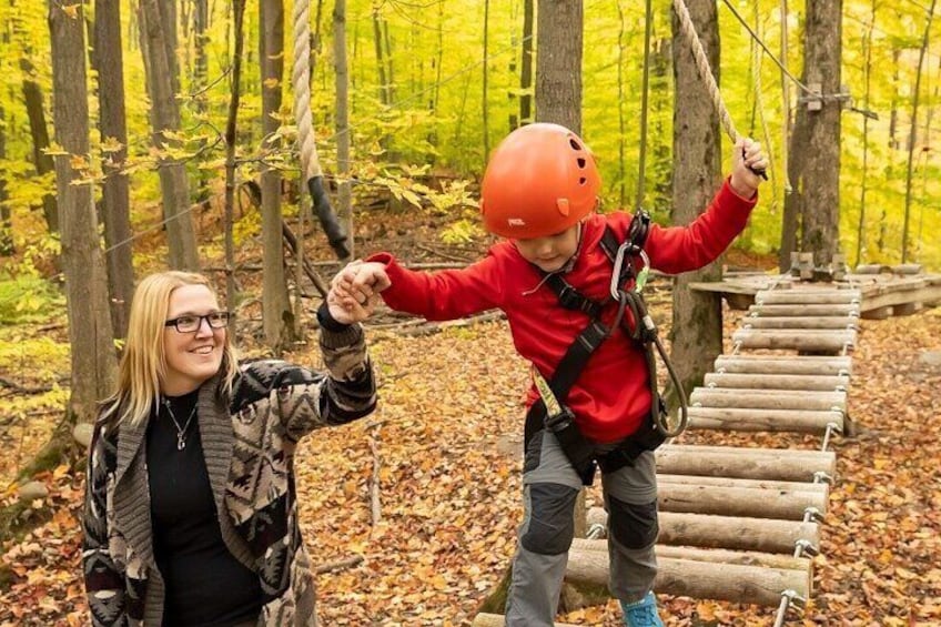 A person in a red jacket and orange helmet navigating a wooden rope bridge in a forest. 4