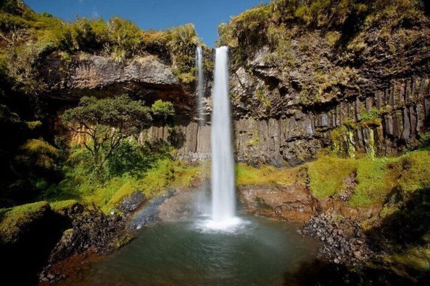 A waterfall cascading into a pool surrounded by rocky cliffs and greenery. 1