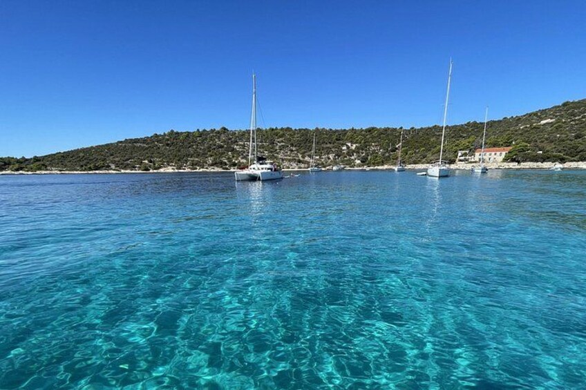 A clear blue sea with sailboats anchored near a hilly coastline. 3
