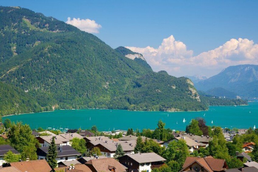 A lake surrounded by mountains, houses along the shore, and sailboats on the water. 4