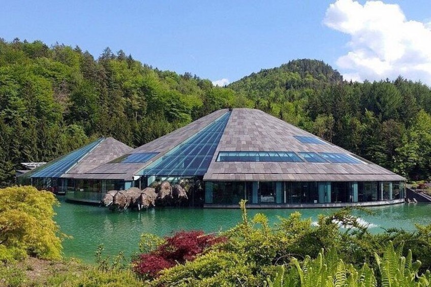 A modern building with a glass roof, surrounded by water and greenery. 4