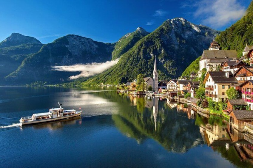 A calm lake with a boat, a church, and traditional buildings reflecting on the water. 1