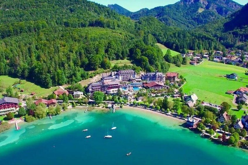 A coastal resort with a large building complex, a clear turquoise bay, and surrounding forested hills. 2