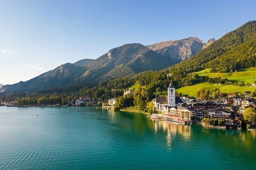 A lake with a church and buildings on the shore, surrounded by mountains. 2