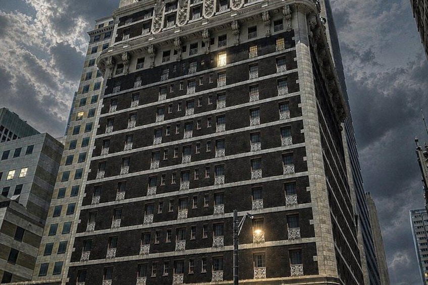 A tall, multi-story building with a dark facade and numerous windows, under a cloudy sky. 3
