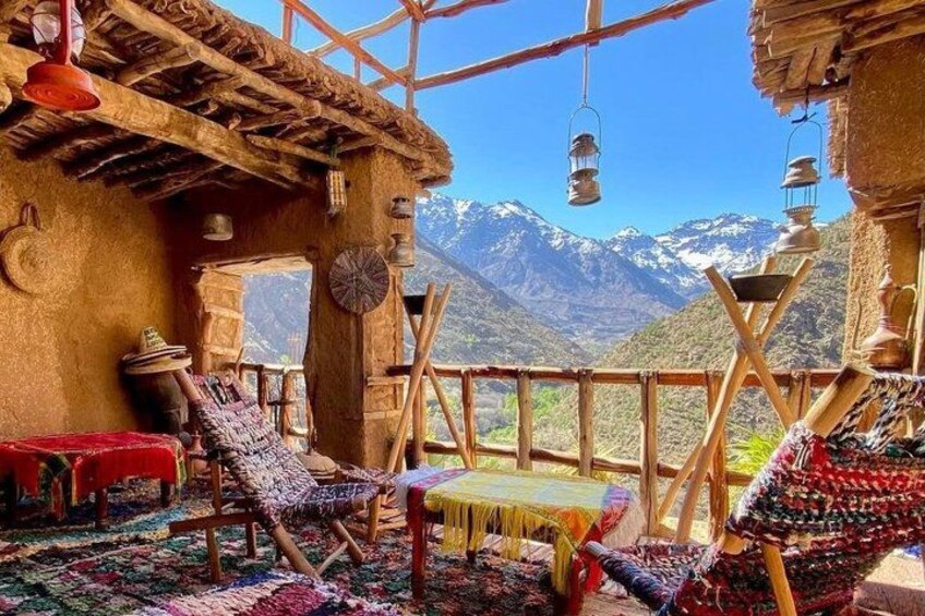 A traditional wooden structure with a thatched roof, colorful woven rugs, and a view of snow-capped mountains. 1