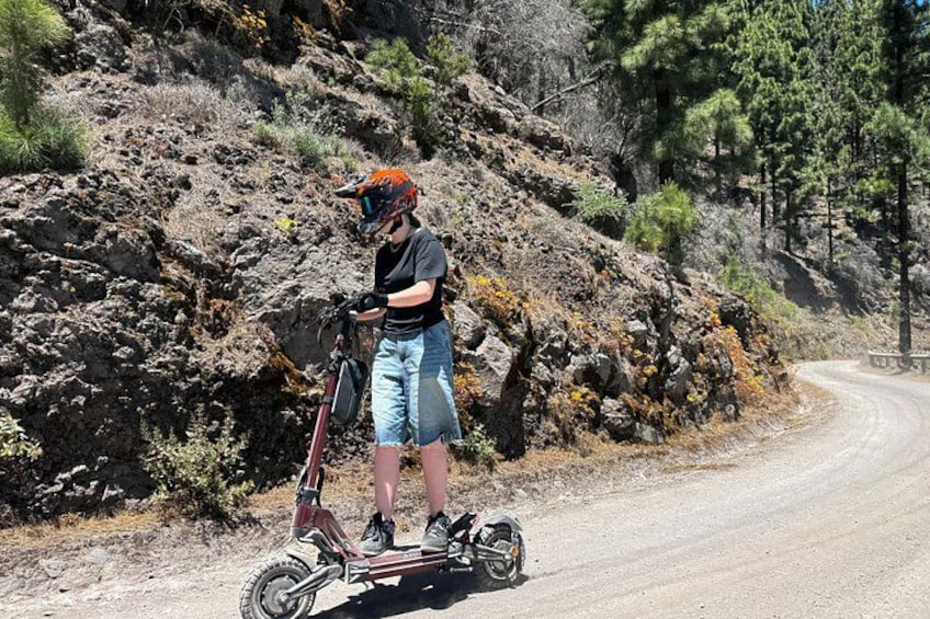 A person on a three-wheeled electric vehicle on a dirt road with rocky terrain and sparse vegetation. 2