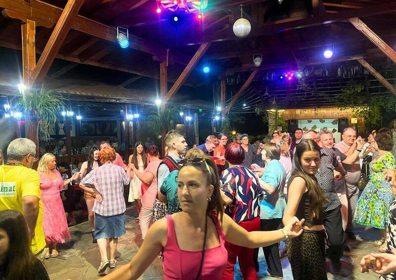 A crowded outdoor dance floor with wooden beams and potted plants. 2