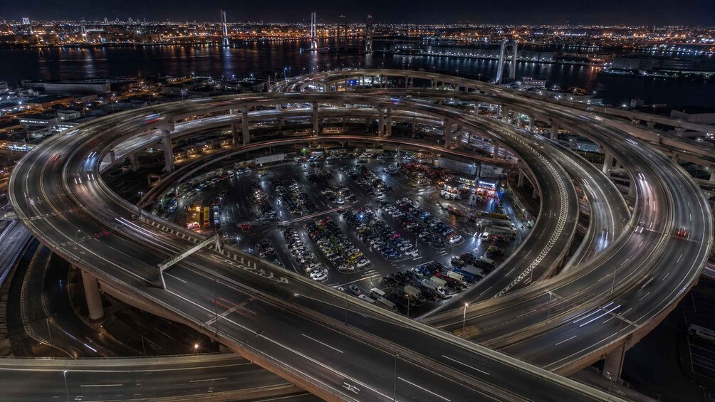 A multi-level highway interchange with vehicles in motion, surrounded by city lights and a body of water. 4
