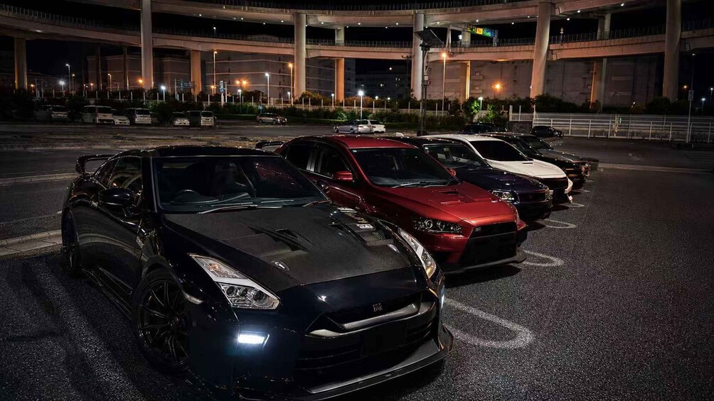 A parking lot at night with several sports cars parked. 1