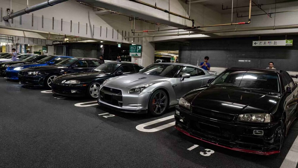 A parking garage with multiple cars, including a black and a silver sports car. 3