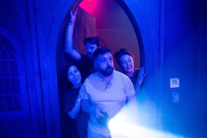 A group of people in a dimly lit room with blue lighting, one person holding a flashlight. 2