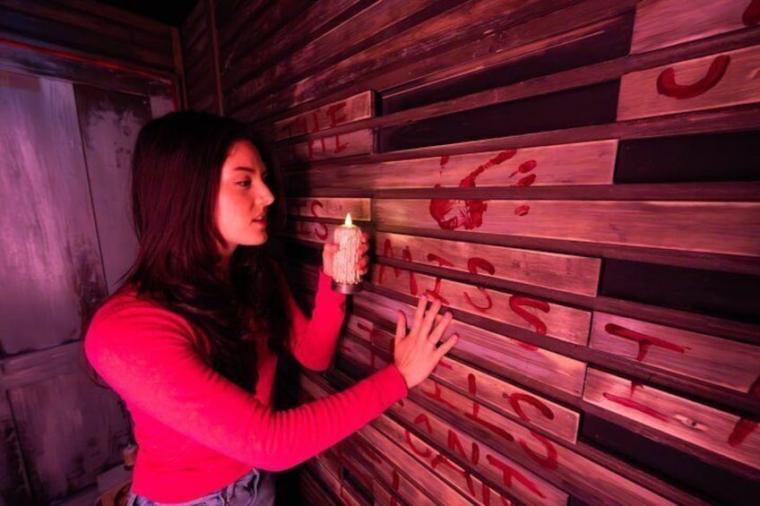 A person holding a candle in front of a wall with wooden planks and red markings. 3