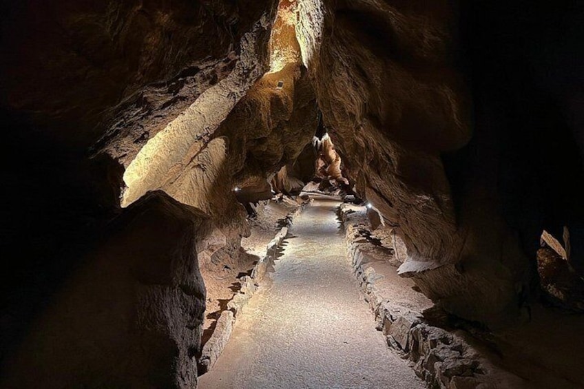 A cave with stalactites and stalagmites, a narrow passageway, and a central light source. 4