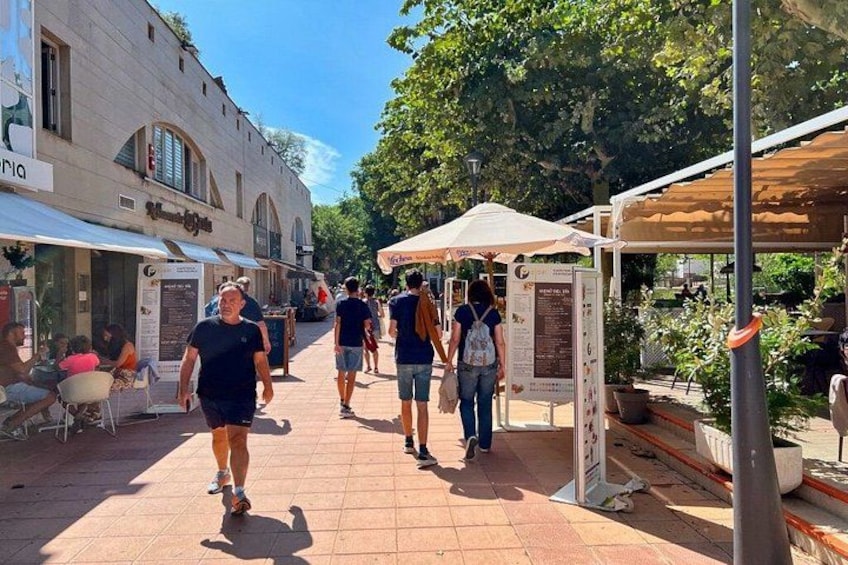 A pedestrian street with people walking, outdoor seating, and covered stalls. 3